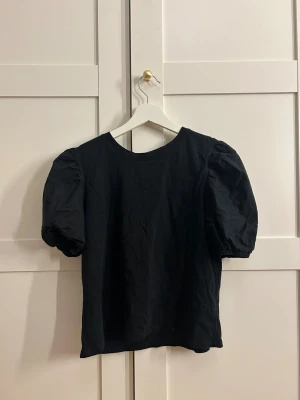 Svart puffärm blus från Zara - Svart blus från Zara med puffiga korta ärmar och rund halsringning. Tillverkad i mjuk bomull som känns skön mot huden. Enkel och stilren design som ger en cool siluett. Perfekt för dig som gillar minimalistiska vibes och vill ha något som sticker ut med volym i ärmarna.