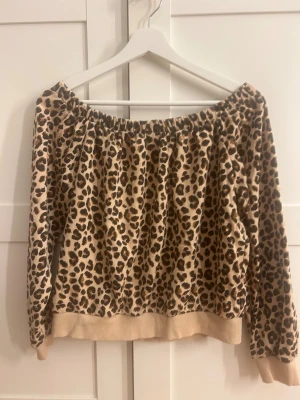 Leopardmönstrad offshoulder tröja M - Säljer en beige och brun leopardmönstrad tröja i storlek M. Tröjan har offshoulder-design med resår runt halsen och långa ärmar. Mjuk insida och ribbade muddar vid ärmslut och nederkant. Perfekt för dig som gillar djurmönster och vill sticka ut.