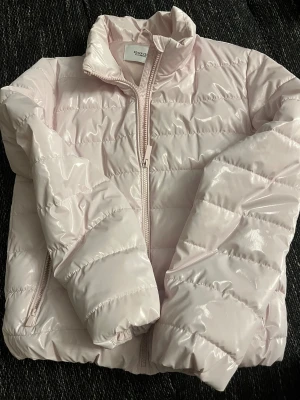 Ljusrosa pufferjacka från Reserved - Säljer en ljusrosa pufferjacka från Reserved med glansig finish och quiltad design. Jackan har hög krage, dragkedja framtill och långa ärmar. Perfekt för dig som vill ha en snygg och mysig jacka med modern vibe.