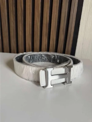 Vit skinnbälte med H-spänne - Snyggt vitt bälte i skinn med ett stilrent H-format metallspänne i silver. Perfekt accessoar för att lyfta din outfit med en clean och modern look. Bältet har en klassisk form och passar till både jeans och kostymbyxor.