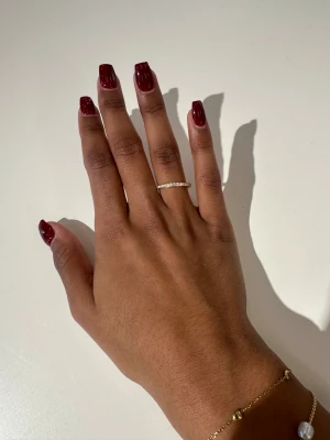 Glittrig guldring  - Snygg tunn guldring från Glitter, pläterad med 18 karat guld och dekorerad med gnistrande cubic zirconia-stenar runt hela ringen. Materialet är rostfritt stål med guldfinish.