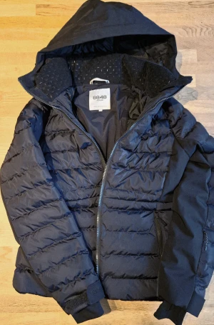 Skidjacka 8848 Altitude Ny utan etikett - Säljer en blå/svart skidjacka från 8848 Altitude med huva och dragkedja. Jackan har quiltad design, två sidofickor med dragkedja och justerbara ärmslut med kardborre. Snölås, liftkortsficka på vänster ärm och två innerfickor. Perfekt för sköna skiddagar och med riktigt snygg passform.
