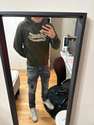 Grön hoodie från Gant med brodyr - Mörkgrön hoodie från Gant i 100% bomull med stor vit broderad logga på bröstet. Klassisk känguruficka framtill och huva med dragsko. Skön och avslappnad passform, perfekt för chill dagar. En mini defekt på bild 3, syns inte vid användning alls. Jag är 181 72kg, BVSA!