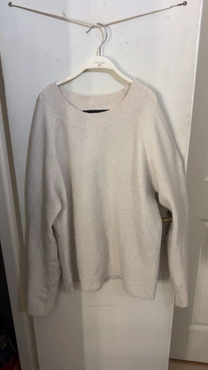 Beige stickad tröja med rund hals - Mysig beige stickad tröja med rundad hals och ribbade muddar vid ärmslut och nederkant. Tröjan har en loose passform och är perfekt för lager-på-lager under kyliga dagar. Enkel och stilren design som funkar till jeans eller kjol.