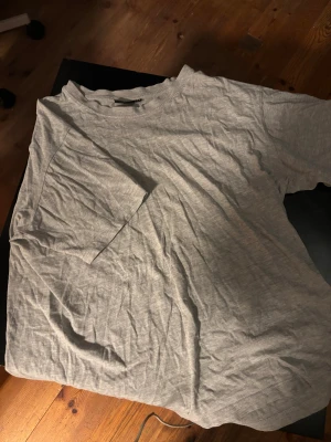 Grå basic t-shirt från Cotton Line - Enkel och stilren grå t-shirt från Cotton Line i storlek M. T-shirten har rund halsringning och korta ärmar, perfekt för en clean och avslappnad look. Tillverkad i mjuk bomull som känns skön mot huden. Finns dock ett pytte litet hål i tröjan