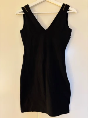 Svart kort klänning med dragkedjedetalj från Zara - Snygg svart miniklänning från Zara med v-ringning både fram och bak, med en cool dragkedjedetalj längs v-ringningen bak. Figurnära passform, storlek S.