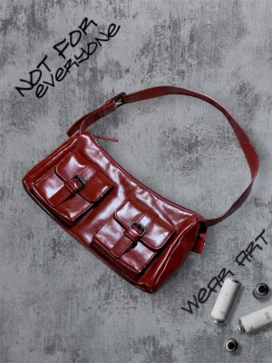 Röd axelväska  - Snygg röd axelväska i skinn med två framfickor som har coola spänndetaljer. Väskan har en justerbar axelrem och stängs med dragkedja upptill. Perfekt storlek för det viktigaste och ger en edgy vibe till din outfit. Lite skav men ser riktigt snygg ut. Färgen är vinröd/röd