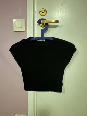 Svart croppad topp från Zara - Säljer en svart croppad topp från Zara. Toppen har en stilren och enkel look som är lätt att matcha med olika outfits. Perfekt för dig som gillar minimalistisk stil och vill ha en topp som sticker ut med sin form.