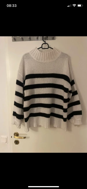 Randig stickad polotröja i vitt och svart - Säljer en oversized stickad polotröja med breda svarta och vita ränder. Tröjan har halv hög ribbad krage, långa ärmar och ribbade muddar. Perfekt för dig som gillar en chill och trendig look under höst och vinter.