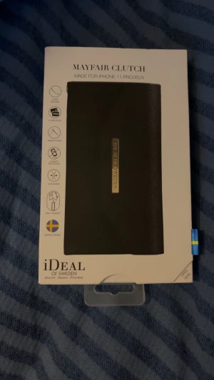 Svart Mayfair Clutch från iDeal of Sweden - Snygg svart Mayfair Clutch för iPhone 11 Pro/XS/X från iDeal of Sweden. Stilren design med guldfärgad logga, tre kortfack och avtagbar handledsrem. Väskan är tillverkad i syntetmaterial med struktur och har magnetstängning. Perfekt för dig som vill ha både mobil och kort samlat.