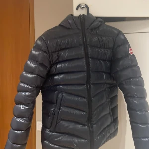 marinblå dunjacka från Colmar - Säljer en snygg svart dunjacka från Colmar. Jackan har en quiltad design med dragkedja och huva. Perfekt för kyliga dagar och ger en stilren look. Den är långärmad och har en klassisk passform. det ända som är lite off är hålet på ryggen, det är lagat med någon lagnings tejp så knappt syns när man ha på sig den skriv dm för fler frågor och bilder, Nypris 3699kr men mitt pris 800kr, storlek 14y