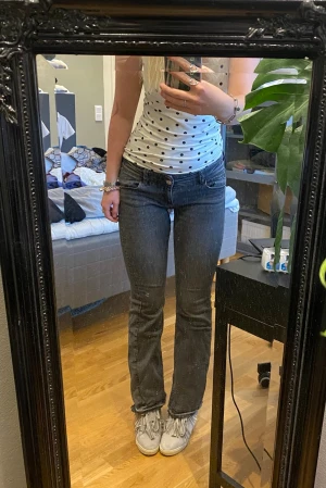 Mörkgrå bootcut jeans med fickdetaljer - Säljer ett par mörkgrå jeans med bootcut passform och snygga fickor med knappdetaljer bak. Jeansen har låg midja och är gjorda i klassiskt denimtyg. Perfekta till sneakers eller boots. De är uppsprättade längst ner för att förlänga innerbenslängden.