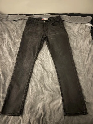 Levi's 512 Slim Taper svarta jeans - Säljer ett par svarta Levi's 512 Slim Taper jeans med klassisk femficksdesign och smal passform. Jeansen har en snygg tvättad look och är tillverkade i bomull med lite stretch för extra komfort. Perfekta för dig som gillar en modern och clean stil.