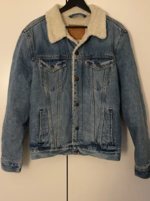 Levi's jeansjacka storlek M - Säljer en  ljusblå jeansjacka från Levi's med vitt teddyfoder. Jackan är i mycket bra skick och i storlek M. Passar perfekt nu när det är rätt så kallt. Priset är ej hugget i sten och det är bar att skriva om du har frågor.