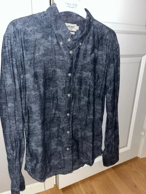 Blommig blå skjorta från East West - Snygg blå skjorta från East West med diskret blommigt mönster. Skjortan har klassisk krage, vita knappar framtill och långa ärmar. Perfekt för dig som vill ha en unik men stilren look. Slim fit. 