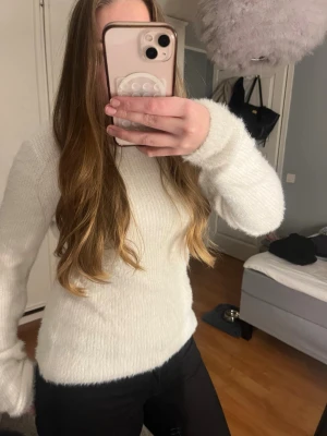 Vit stickad tröja med öppen rygg och knyt - Supermysig vit stickad tröja med lång ärm och öppen rygg som knyts med en rosett. Tröjan har en lätt fluffig känsla och sitter snyggt med normal passform. Perfekt för kyligare dagar när du vill vara både bekväm och stilren.