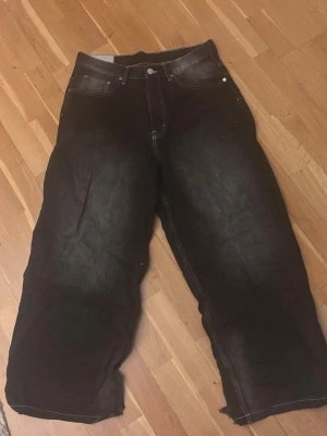 Svarta baggy jeans - Säljer ett par svarta jeans med bred passform Jeansen har klassisk femficksdesign, vita kontrastsömmar och en riktigt baggy vibe. Perfekta för dig som gillar oversized och streetwear. Materialet är robust denim. Har lite heeldrag
