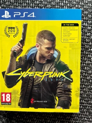 Cyberpunk 2077 PS4 - Cyberpunk 2077 till PS4, komplett med 2x Blu-ray disc, världskompendium, klistermärken, vykort, spelkarta och digitalt innehåll. Omslaget är i fint skick, perfekt för samlare eller spelentusiaster.