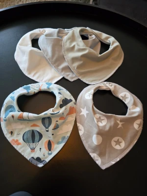 Fem mjuka haklappar i bomull - Säljer fem haklappar/dregglisar i mjuk bomull, perfekta för småbarn. Tre är enfärgade i vitt och sage och beige, en har stjärnor och prickar i vitt på beige botten, och en har ballongmönster i blått, orange och beige. Alla har tryckknapp för enkel användning. Fleecebaksida vilket ger mycket bra skydd mot dreggel. 