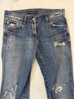 Dolce & Gabbana blå slitna raka jeans - Säljer ett par blå jeans från Dolce & Gabbana med slitningar och trasiga detaljer framtill och baktill. Jeansen har raka ben och klassisk femficksdesign. Dessa är as snygga men passar inte mig tyvärr! Midjemått 39cm och innerbenslängd 82cm.🫰🫰