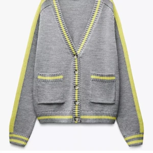 Grå kofta med gula ränder - SÖKER!!!! En grå kofta med gula och ljusgrå ränder längs kanterna, ärmarna och fickorna. Koftan har v-ringning, knappar framtill och två fickor.