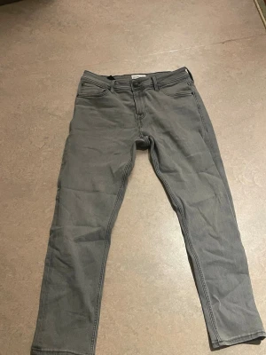 Grå jeans från Stock & Hank - Säljer ett par grå jeans från Stock & Hank. De har klassisk femficksdesign, normal passform och raka ben. Jeansen är tillverkade i bomull med en mjuk känsla och har bälteshällor samt knapp- och dragkedjestängning. Perfekta till en avslappnad stil.