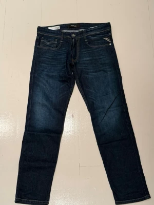 Mörkblå Replay Anbass jeans - Säljer ett par mörkblå Replay Anbass jeans med klassisk femficksdesign och snygga kontrastsömmar. Jeansen har normal passform och raka ben, tillverkade i mjukt jeansmaterial. Märkespatch bak i midjan och diskret Replay-detalj vid fickan framtill.w31:l30