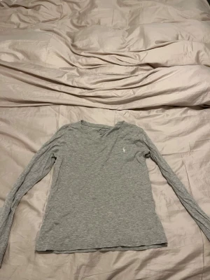 Grå långärmad topp från Polo Ralph Lauren - Säljer en stilren grå långärmad topp från Polo Ralph Lauren. Toppen har rund halsringning och en liten broderad logga på bröstet. Tillverkad i mjuk bomull som är skön mot huden. Perfekt att matcha med jeans eller kjol för en enkel och snygg look.