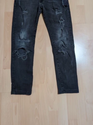 Svarta skinny jeans med slitningar - Säljer ett par svarta skinny jeans från Denim i storlek 29. Byxorna har flera slitningar och hål framtill för en riktigt edgy look. Modellen är tight och smal hela vägen ner. Perfekta för dig som gillar streetstyle och vill ha ett par jeans som sticker ut.