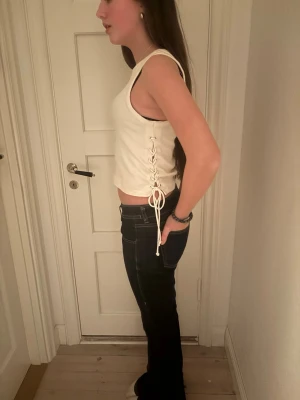 Vit ribbad linnetopp med snörning - Säljer en vit croppad linnetopp med ribbad struktur och snygg snörning i sidan. Toppen är ärmlös och har en enkel, stilren design som passar perfekt till jeans eller kjol. Perfekt för varmare dagar och till fest