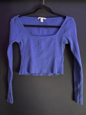 Blå ribbad topp från H&M - Säljer en blå ribbad topp från H&M i storlek S. Toppen har lång ärm, croppad passform och en bred, fyrkantig urringning. Perfekt att styla med höga jeans eller kjol för en trendig look.