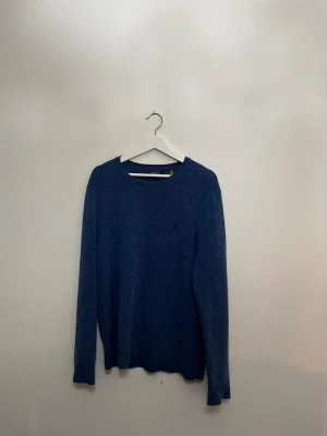 Blå stickad tröja från ralph lauren - Mysig blå stickad tröja från Polo Ralph Lauren med disk iför logga på bröstet. Klassisk rund halsring tracks och långärmad modell som passar perfekt till jeans eller kjol. Enkel och stilren design som funkar året runt.