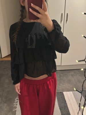 Svart blus med volager  - Strl 152 (xxs, xxxs)  lite genomskinlig längst ner. Använd ett få tal gånger. Inga fläckar, passar bra om man vill ha en lite kortare blus!