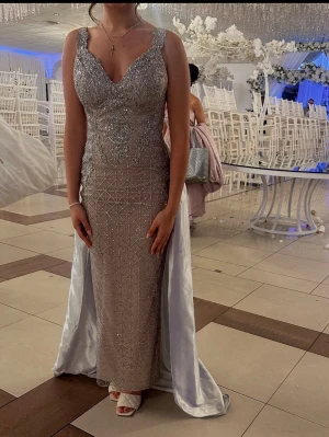 Silverglittrig långklänning med öppen rygg - Säljer en elegant långklänning i rosa och silver med glittriga detaljer och geometriskt mönster. Klänningen har v-ringning, breda axelband och en riktigt snygg öppen rygg. Materialet är glittrigt och skimrande, med ett borttagbart släp i satin tyg som ger extra wow-effekt.