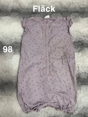 lila prickig byxdress stl 98 - Söt lila byxdress med små svarta prickar och korta puffärmar. Knäppning framtill och resår vid benslut för en bekväm passform. Perfekt för varma dagar och enkel att ta på. 🌸 Fläck. Storlek 98
