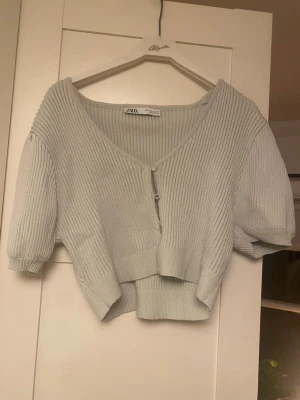 Mintgrön ribbad kofta från Zara - Kort, mintgrön ribbad kofta från Zara med v-ringning och knappar framtill. Tröjan har puffiga korta ärmar och bred mudd i nederkant. Supergullig men kommer inte till användning🫶liten i storleken så skulle säga att den passar S/M mer