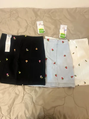 Kjolar  - Säljer tre stycken jeanskjolar. En vit med solrosblommor och en dragkedja vid sidan, en svart med färgade svampar på och en dragkedja vid sidan och en blå med vattenmelon på med en dragkedja på sidan. 