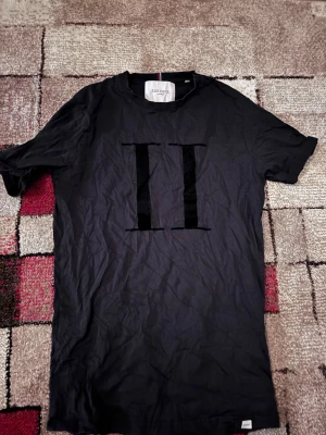 Svart t-shirt från Les Deux - Snygg svart t-shirt från Les Deux med stor sammetsapplikation i form av två romerska siffror II på bröstet. Klassisk rund halsringning och korta ärmar. Tillverkad i mjuk bomull för skön känsla och stilren look.