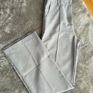 Ljusgrå kostymbyxor med raka ben - Snygga ljusgrå kostymbyxor med raka ben och pressveck. Byxorna har fickor i sidorna och hällor för bälte. 