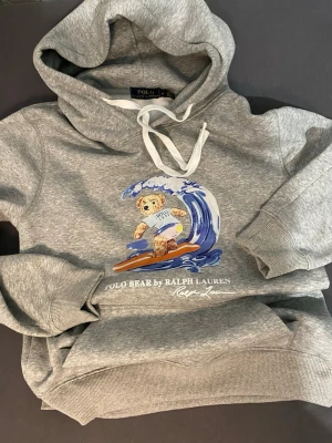 Ralph Lauren hoodie  - Ralph Lauren hoodie i grå färg, med tecknad bild i mitten. I nytt skick, använd en gång bara. Storlek M men passar S också. 