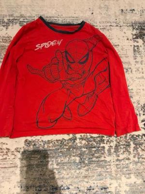 Röd långärmad Marvel Spiderman t-shirt - Cool röd långärmad t-shirt från Marvel med stor Spiderman-tryck på framsidan och svart kontrastkant vid halsen. Perfekt för dig som älskar superhjältar och vill sticka ut med en snygg och bekväm tröja.