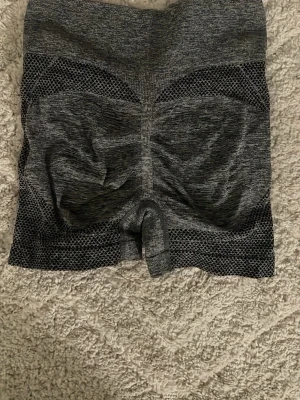 Grå träningstights shorts - Säljer ett par gråa träningstights shorts med hög midja och mesh-detaljer. De är tillverkade i ett stretchigt syntetmaterial som sitter tight och formar sig efter kroppen. Perfekta för gymmet eller löpning. Helt nya