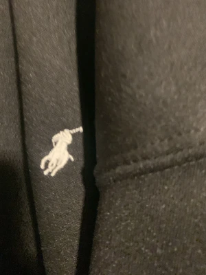 Svart t-shirt från Ralph Lauren - Svart t-shirt från Ralph Lauren med den klassiska broderade vita polospelaren på bröstet. Enkel och stilren design, perfekt för dig som gillar ikoniska märken och en clean look. T-shirten är i mjuk bomull och har en normal passform.