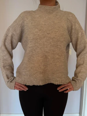 Beige stickad med ribbade detaljer  - Mysig beige stickad med hög ribbad krage. Tröjan har även ribbade detaljer vid ärmslut och nederkant. Perfekt för kyliga dagar när du vill vara både bekväm och snygg. 💕💕