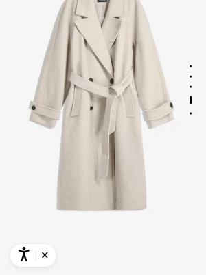 Beige lång kappa med bälte - Snygg beige kappa med klassisk krage och breda slag. Jackan har dubbelknäppning, bälte i midjan och dekorativa knappar vid ärmslut. Tillverkad i ett mjukt ullmaterial som ger en lyxig känsla. Perfekt för dig som vill ha en stilren och tidlös look. Ordpris 700kr, den är oanvänd så säljer för 550kr men kan gå ner i pris vid snabb affär! 