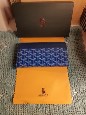 Blå Goyard plånbok med mönster - Snygg blå plånbok från Goyard med deras ikoniska grafiska mönster i vitt och blått. Plånboken har dragkedja runtom, flera fack för kort och mynt samt detaljer i skinn. Perfekt för dig som vill ha något unikt och lyxigt i väskan.