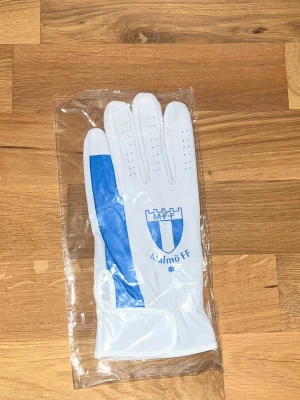 Malmö FF vita och blå fotbollshandskar - Snygga vita fotbollshandskar med blå detaljer och Malmö FF-logga på ovansidan. Handskarna har perforeringar för ventilation och kardborreknäppning vid handleden. Perfekta för dig som vill visa ditt stöd för laget på planen. Storlek: Meidum om man vill ha small går finns det också!