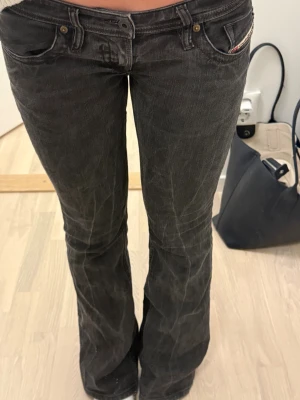 Svarta bootcut jeans med broderi - Säljer ett par svarta jeans med bootcut passform och låg midja. Jeansen har snygga broderade detaljer på bakfickorna och klassisk femficksdesign. Materialet är jeans och färgen är mörk, vilket ger en cool och avslappnad vibe.