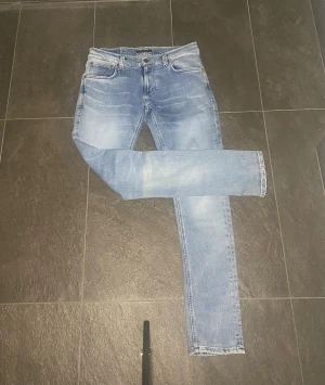 Ljusblå Nudie Jeans  - Säljer ett par ljusblå jeans från Nudie Jeans i nytt skick i storleken 30/32. De har klassisk femficksdesign, raka ben och snygga slitningar framtill. Jeansen är tillverkade i mjukt bomullsmaterial och har en normal passform med medelhög midja. Hör av dig vid frågor eller prisförslag!🤝