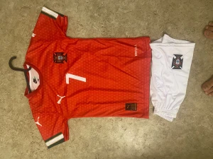 Portugal Ronaldo fotbollströja set - Säljer ett Portugal fotbollströja set med Ronaldo #7. Tröjan är röd med vita detaljer, små mönster och landslagsemblem på bröstet. Vita shorts med emblem ingår. Materialet är lätt polyester, perfekt för fotbollsträning eller match.